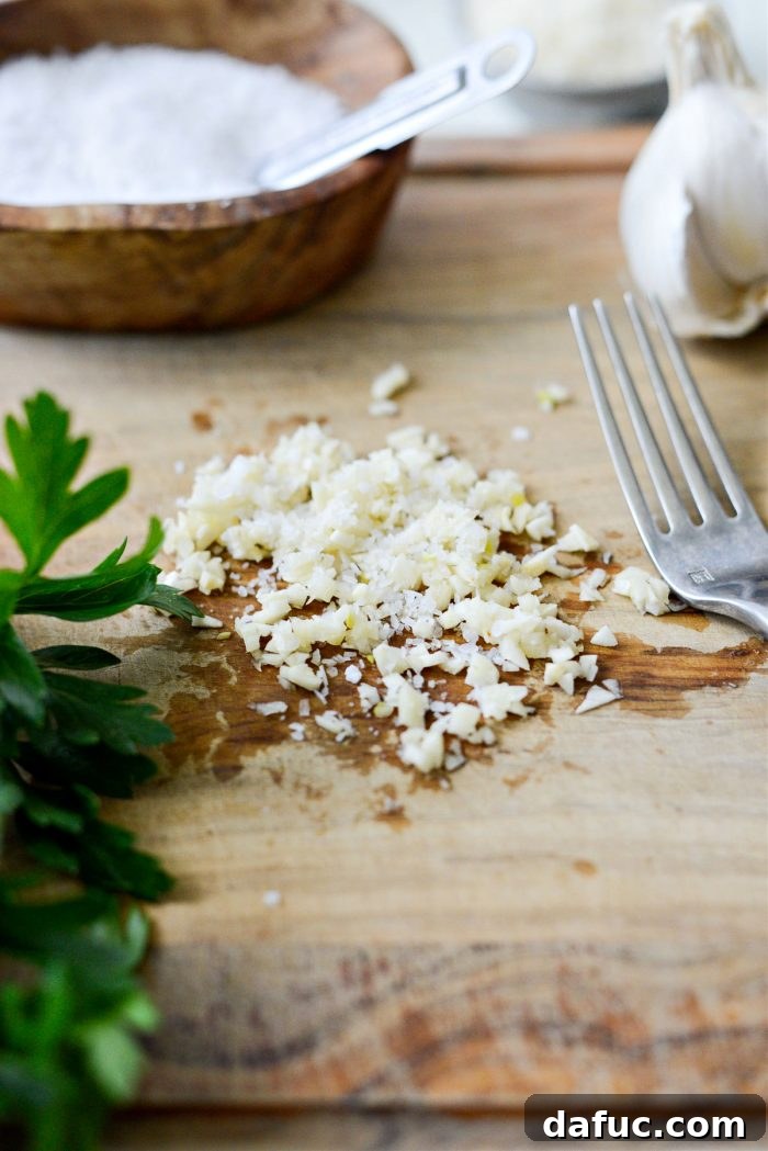 Close-up of minced garlic and kosher salt on a cutting board, ready to be mashed into a paste
