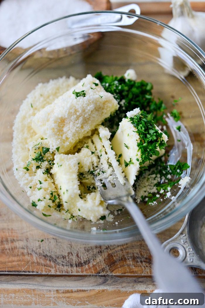 A fork mixing softened butter, garlic paste, parmesan cheese, and fresh parsley in a bowl