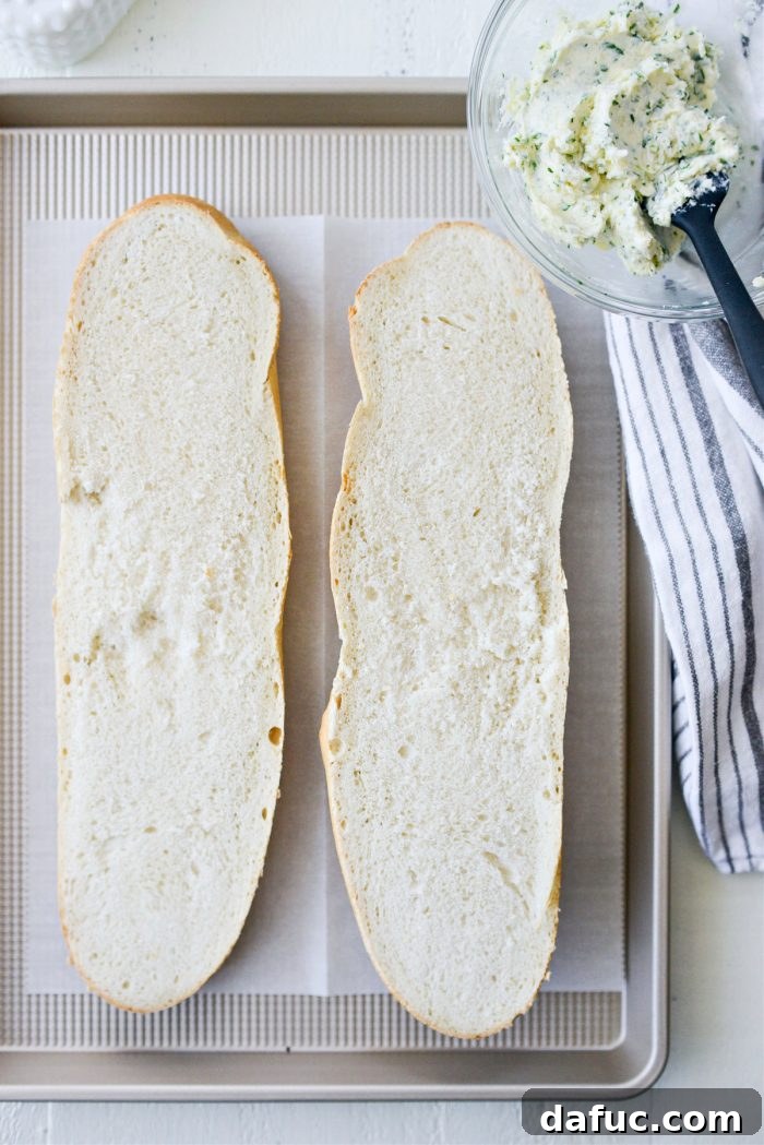 A loaf of Italian bread sliced neatly in half horizontally, placed on a parchment-lined baking sheet