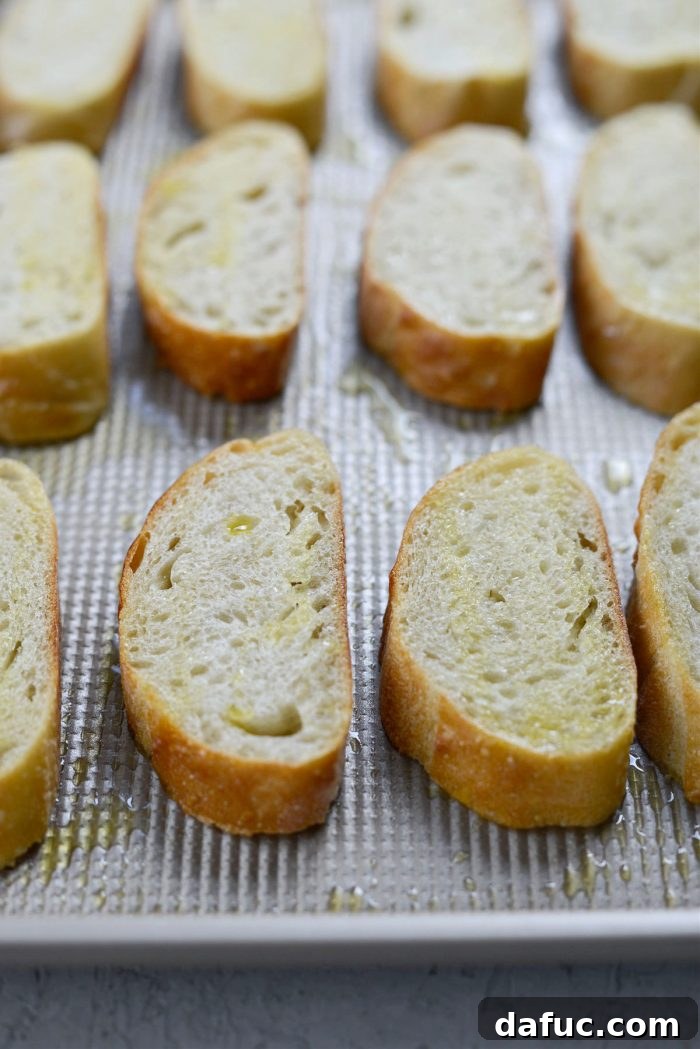 Slices of French baguette arranged on a baking sheet before toasting.