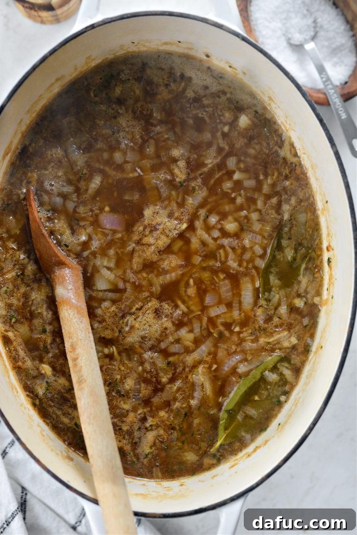 The deeply colored, aromatic French onion soup simmering gently in a Dutch oven.