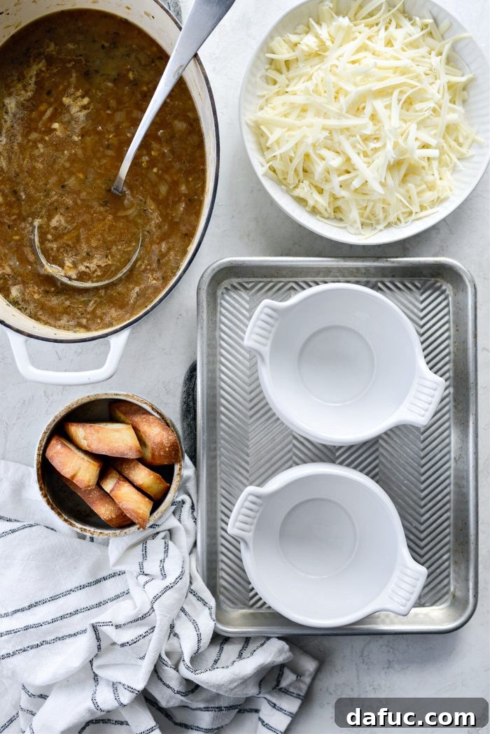 A soup assembly station with a pot of soup, toasted baguette, grated Gruyère, and oven-safe bowls.