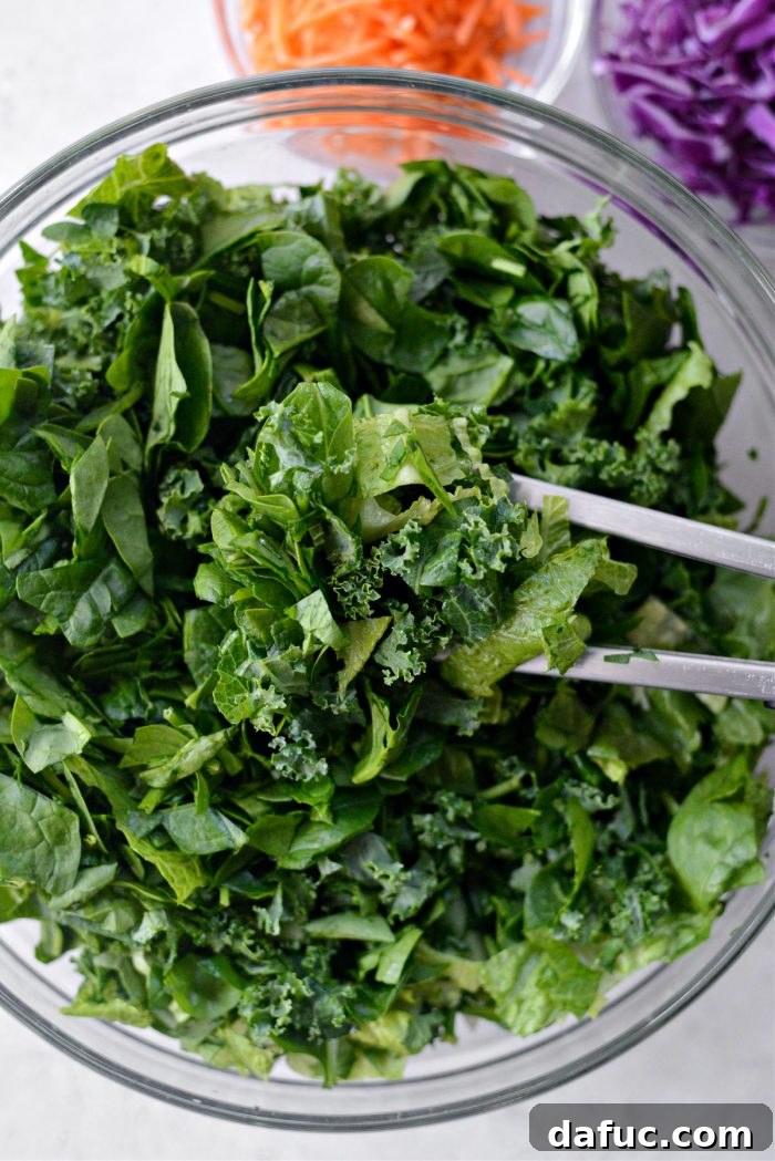 Close-up of a hand using tongs to gently toss the mixed greens in a large bowl.