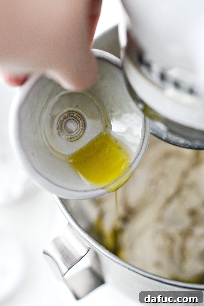 Adding olive oil to the dough in the mixer.