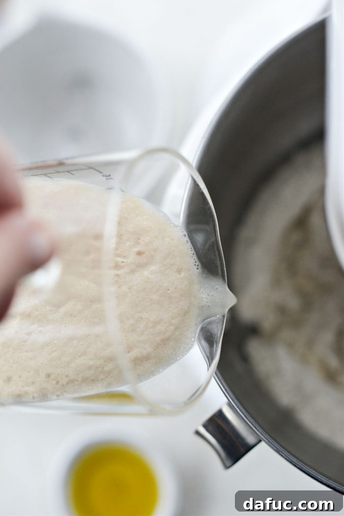 Pouring bloomed yeast mixture into the stand mixer with dry ingredients.