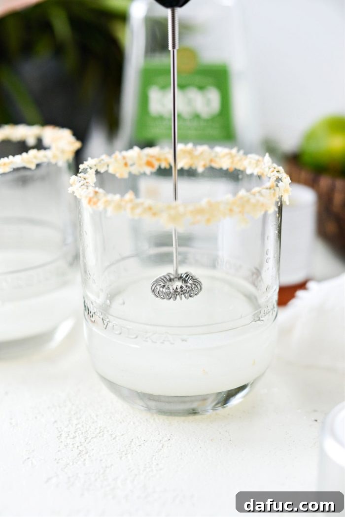 A mini electric whisk being used to blend the coconut tequila and cream of coconut in a glass