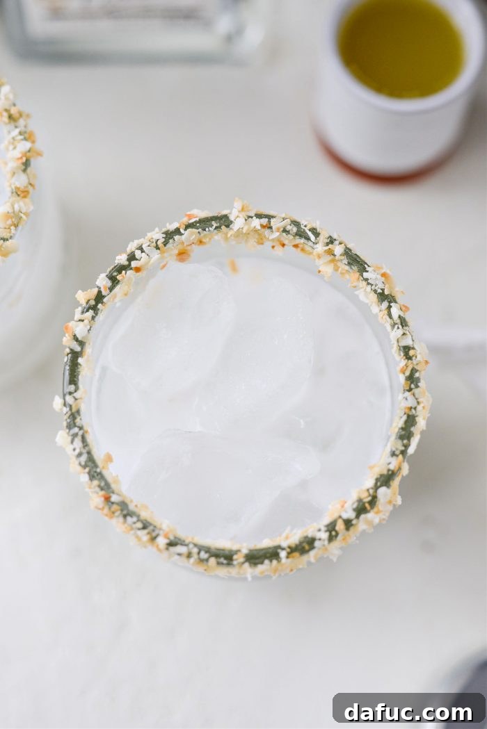 Ice cubes being added to the frothy coconut tequila and cream of coconut mixture in the glass