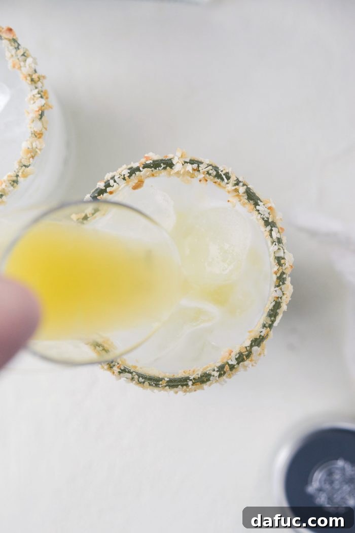 Pineapple juice being poured over the ice and blended cocktail mixture, completing the Pina Colada Margarita