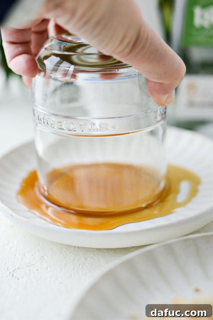 A glass being dipped into maple syrup or agave on a shallow plate to prepare for the toasted coconut rim