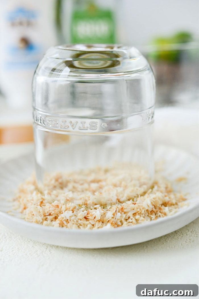 The rim of a glass, already coated in syrup, being dipped into the finely ground toasted coconut