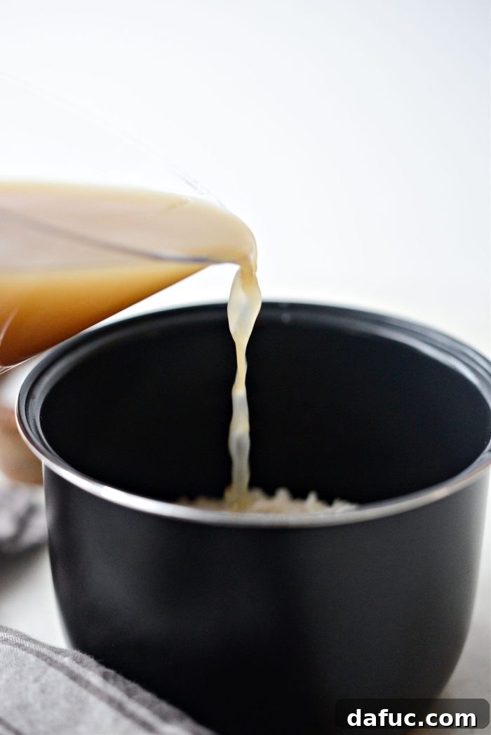 Pouring chicken bone broth into a rice cooker with rice